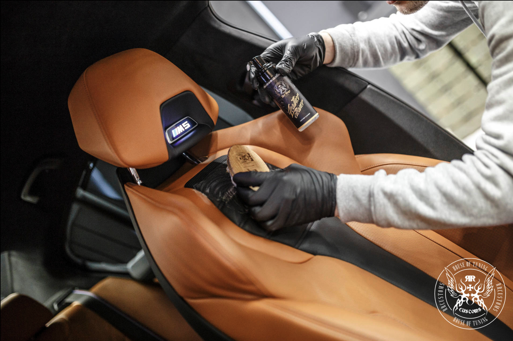 Leather Care Set – Vista de cima da mão com luva a usar escova redonda no painel de porta de couro laranja-caramelo | Cuidado do Couro | miio Store