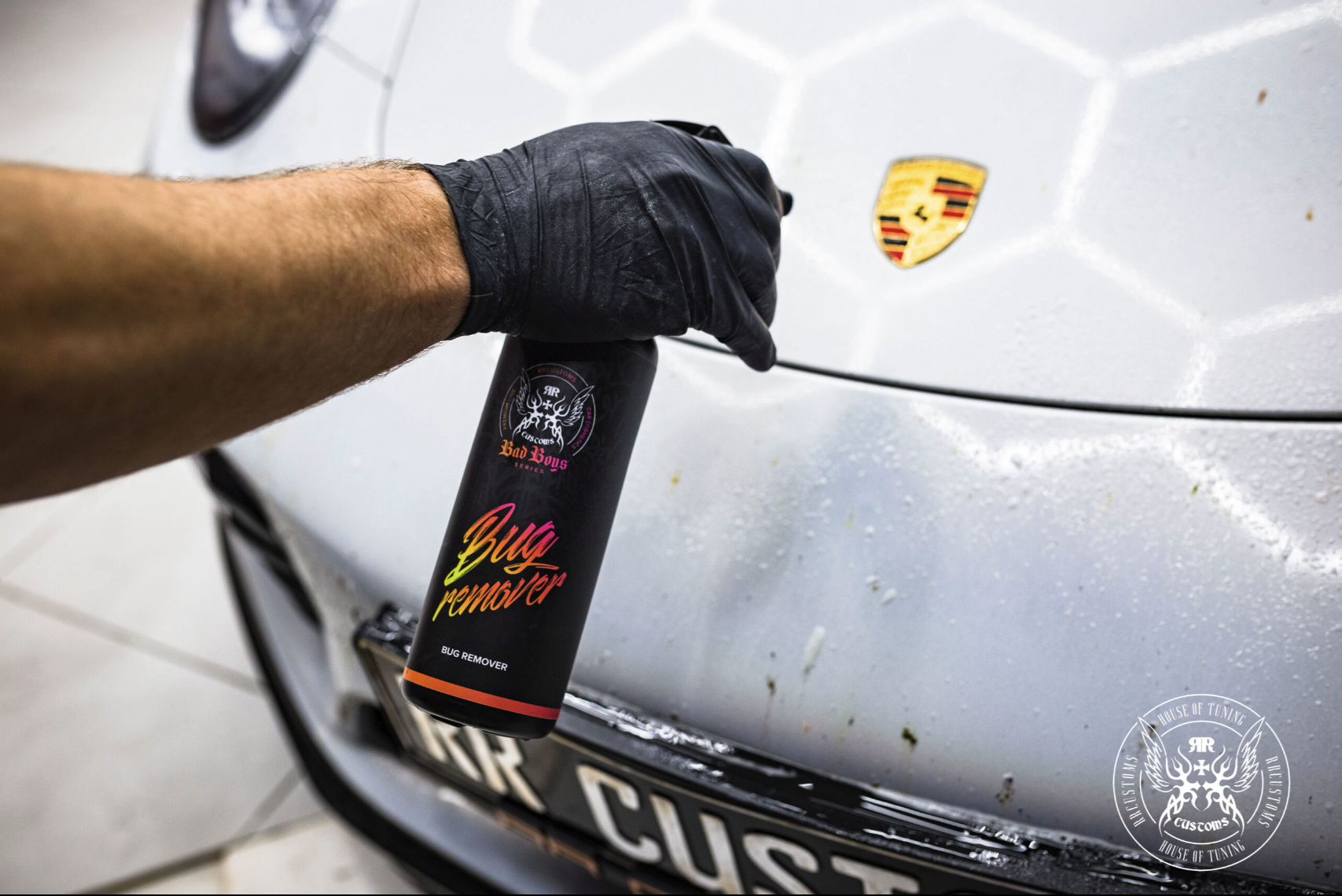 Bug Remover 1L – Main gantée vaporisant produit sur capot gris avec badge Porsche visible au studio JK Customs | Detailing Auto | miio Store