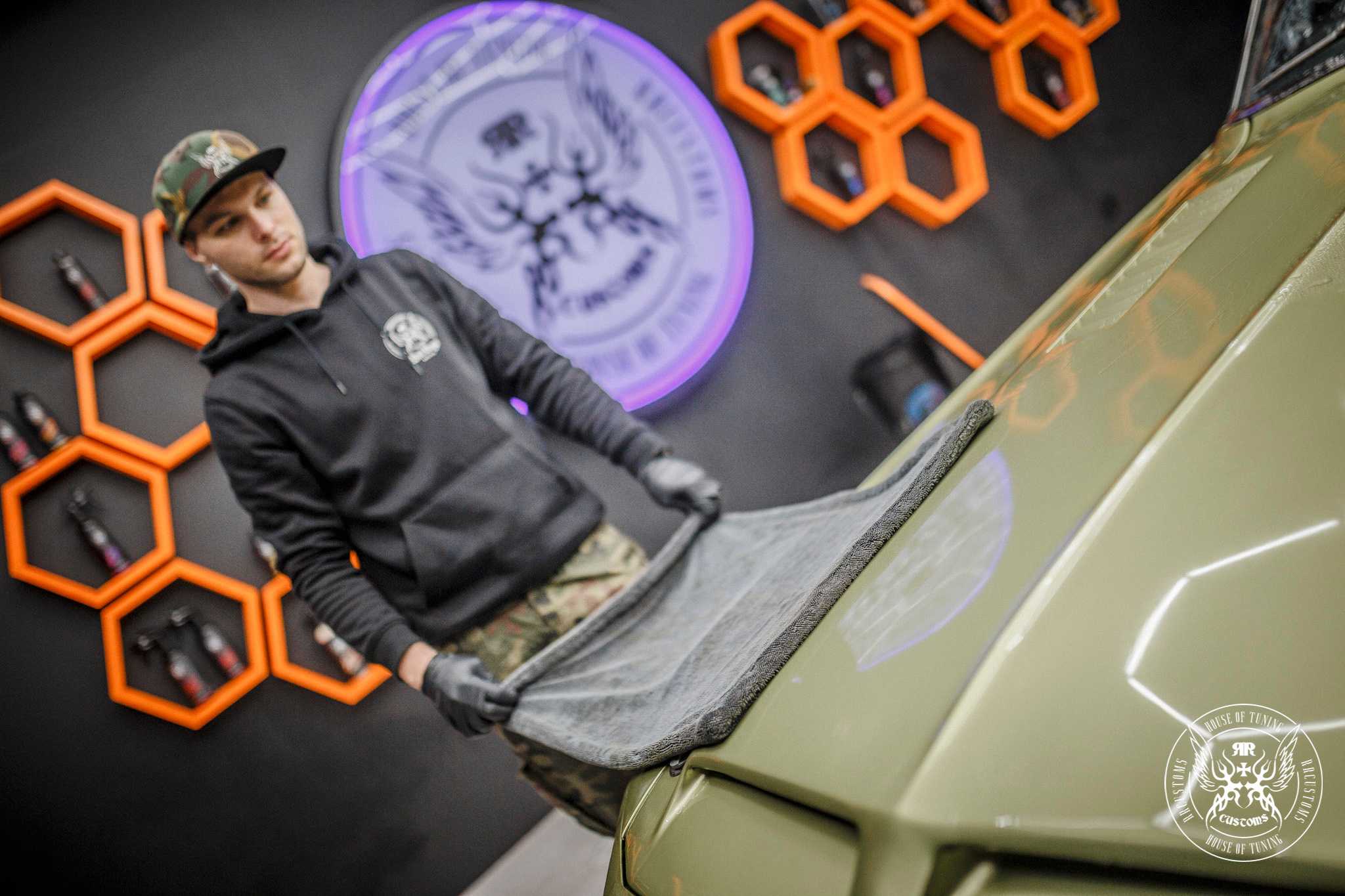 Black Master Drying Towel – Hombre con gorra usando la toalla premium gris oscura para secar capó de coche verde militar en estudio hexagonal naranja | Detailing Auto | miio Store