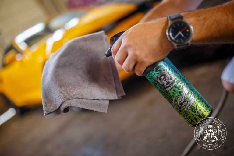 Ceramic Detailer 500ml – Mão com relógio a usar microfibra cinza para aplicar ceramic detailer em pintura de carro amarelo, close-up | Detailing Auto | miio Store