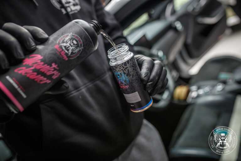 Alcantara Cleaner – Mãos com luvas pretas a pulverizar produto diretamente em revestimento de alcântara escuro | Interior Auto | miio Store