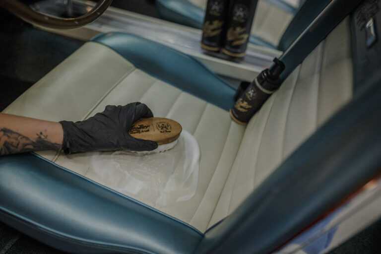 Leather Cleaner – Close-up de mão com luva preta com escova redonda a escovar superfície de assento de couro creme | Cuidado do Couro | miio Store